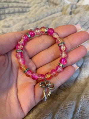 Rosa pärlarmband med baletthänge - Snyggt armband med glittrande rosa och orange pärlor, dekorerat med silvriga detaljer och ett hänge i form av balettskor. Perfekt accessoar för dig som gillar färg och dansinspirerade smycken.