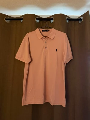 Ljusrosa pikétröja från Ralph Lauren - Säljer en ljusrosa pikétröja från Ralph Lauren med klassisk krage och knappar framtill. Tröjan har korta ärmar och den ikoniska broderade loggan på bröstet. Perfekt för en clean och stilren look.