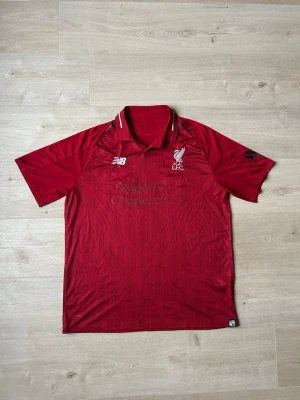 Liverpool FC Fotbollströja 2018/19 Hemmatröja Storlek L - Mycket fin fotbollströja i röd färg. Tröjan är i mycket bra skick och sparsamt använda. |  Äkta som allt annat jag säljer! ✅ |  Storlek: L | Skick: Mycket Bra Skick - Tyvärr har trycket släppt på sponsortexten och storleksetiketten (SE SISTA 2 BILDER) | Färg: Röd | Märke: New Balance | Modell: Fotbollströja |   Hör gärna av dig vid frågor så svarar jag så fort jag kan! 😄