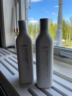 O&M Hydrate & Conquer duo - Säljer ett set med O&M Hydrate & Conquer shampoo och balsam, båda i vita flaskor med stilren design. Varje flaska innehåller 350 ml och är perfekt för dig som vill ge håret extra fukt och näring. Oanvända