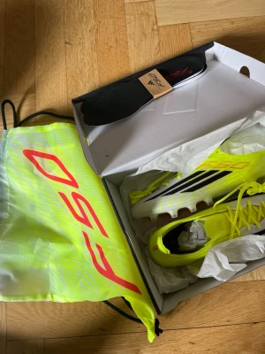 Adidas F50 Elite AG fotbollsskor - Säljer ett par hellt oanvända Adidas F50 Elite AG fotbollsskor i neon-gult med svarta och vita detaljer. Säljer dem på grund av att jag fick dem gratis av min klubb och har andra skor jag använder. Skorna har en modern, strömlinjeformad design och levereras med tillhörande påse och extra innersulor. Perfekta för spel på konstgräs nu när säsongen drar igång. Priset är ej hugget i sten. Ny pris 3099, mitt pris 1500