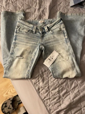 Ljusblå bootcut jeans med brodyr - Säljer ett par ljusblå bootcut jeans med slitningar framtill och snygg broderad detalj på bakfickorna. Jeansen har klassisk femficksmodell, bälteshällor och är i stretchigt denimtyg. Perfekta för en trendig och avslappnad look.