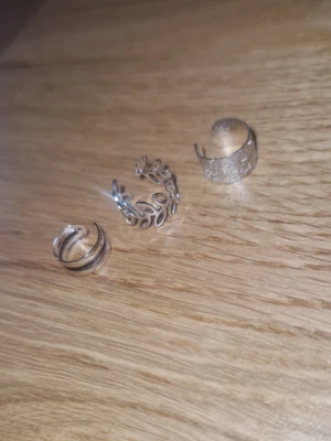 Ear cuffs - Tre helt nya snygga ear cuffs i silverfärgad metall. En har ett glittrigt, brett band, en har ett öppet bladmotiv och den tredje har dubbla tunna ringar. Perfekta för att ge din look lite extra edge utan att behöva hål i öronen.