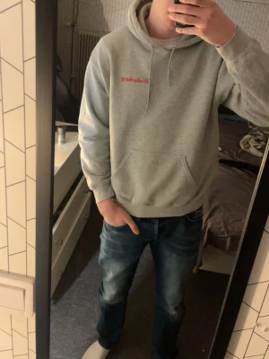 Grå Après Ski hoodie drakenberg - Säljer en grå hoodie med huva och magficka. På bröstet finns en liten röd text och på ryggen ett stort tryck med texten 'APRÈS SKI' och en bild på en tjej med snowboard. Hoodien har ribbade muddar och är i mjukt bomullsmaterial. Perfekt för dig som gillar streetwear och coola prints.