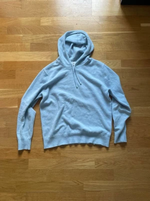 Ljusblå hoodie från Sayless i cashmere - Mysig ljusblå hoodie från Sayless i mjuk cashmereblandning. Klassisk modell med huva, ribbade muddar vid ärmslut och nederkant. Perfekt för en chill och avslappnad stil.