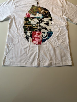 Vit BAPE t-shirt med camo-tryck - Vit t-shirt från BAPE med stort camoflague märke i olika färger helt sprillansny kommer med lappar och tillbehör skicka 10/10 skickas samma dag som köp  