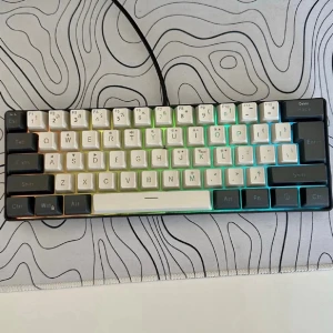 Mekaniskt tangentbord med RGB-belysning - Snyggt mekaniskt tangentbord med svart och vit färgkombination och RGB-belysning. Kompakt layout med svenska tangenter och USB-anslutning. Perfekt för gaming eller skrivarbete. Tangenterna är i plast och har en modern design.
