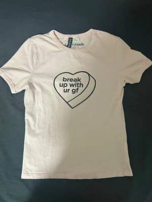 Beige Ariana Grande t-shirt -  beige t-shirt från Ariana Grande med tryck i form av ett hjärta och texten 'break up with ur gf' på bröstet