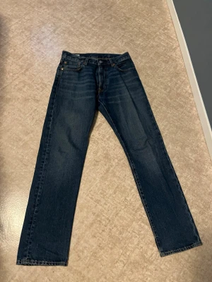 Levi's 551Z raka jeans mörkblå - Mörkblå raka jeans från Levi's, modell 551Z. Klassisk femficksdesign med gylf och knapp, tillverkade i slitstark denim. Perfekta för en avslappnad och tidlös look.
