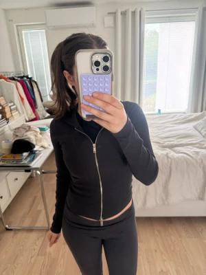 Svart croppad hoodie med dragkedja - Säljer en svart, croppad hoodie med dragkedja framtill och åtsittande passform. Hoodien har långa ärmar och en klassisk huva. Perfekt för en avslappnad och sportig stil.
