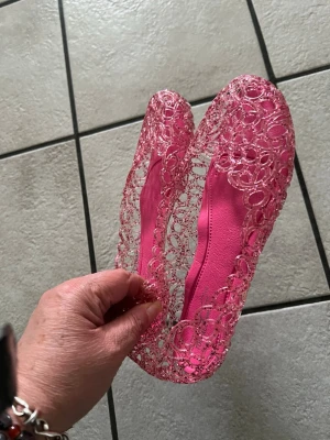Rosa genomskinliga ballerinaskor storlek 37 - Säljer ett par unika rosa ballerinaskor i plast med genomskinligt, spetsliknande mönster. Skorna har rund tå och är superlätta och flexibla. Perfekta för dig som vill sticka ut med färg och cool design.