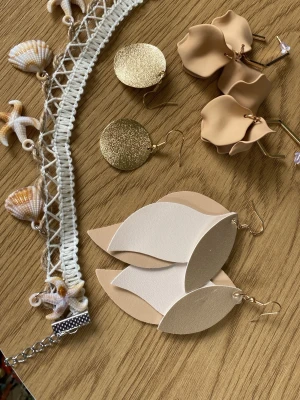Beige och vita bladformade örhängen - Säljer ett par stora, bladformade örhängen i beige och vitt. De är gjorda i mjukt konstläder och har en modern, lager-på-lager design. Örhängena har guldfärgade krokar och passar perfekt för dig som gillar statement-accessoarer.