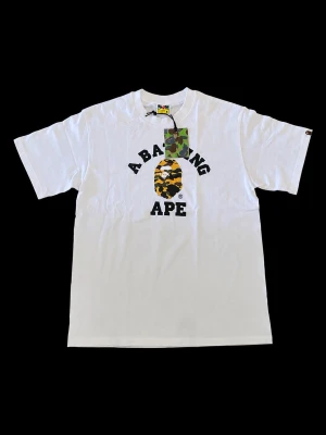Bape T-Shirt - Säljer denna helt ny då den var för liten för mig, det är storlek M. Detta är en tröja från bape med klassiska camo loggan, perfekt för streetwear stilen nu till sommaren. Det är 100 bomull så den är väldigt luftig och skön! #streetwear #opium