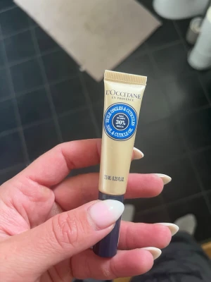 Nagel- och nagelbandsolja L'Occitane - Nagel- och nagelbandsolja från L'Occitane i en beige tub med blå etikett. Innehåller 7,5 ml och har 30% sheasmör för intensiv återfuktning. Perfekt för att vårda torra nagelband och ge naglarna extra glans.