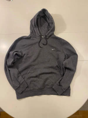 Mörkgrå Nike hoodie S - Säljer en mörkgrå hoodie från Nike med klassisk huva och dragsnören. Hoodien har en stor magficka och den ikoniska vita Nike-loggan broderad på bröstet. Tillverkad i mjukt bomullsmaterial som är perfekt för chill dagar.