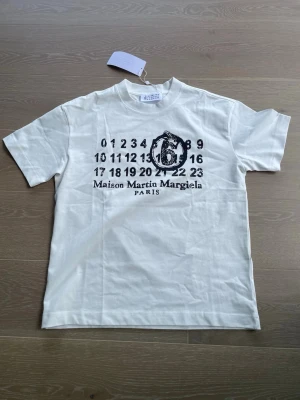 MM6 Maison Margiela Snake Numeric Tee – Off White – Size S – Brand New with tags - MM6 Maison Margiela t-shirt in off-white. Numeric label print on the chest with snake graphic, large snake “6” on the back. Brand new with tags, never worn. Size S but fits oversized – works well on M too. Retail price ~€230. Selling for 700 SEK. Shipping not included, local pickup possible.