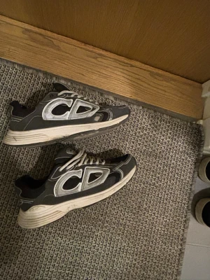 Svarta CD sneakers med vit sula - Snygga svarta sneakers med stora vita CD-bokstäver på sidorna och vit, chunky sula. Skorna har sportig design, svarta och vita detaljer samt klassisk snörning. Perfekta för dig som gillar streetwear och vill sticka ut med en unik look.