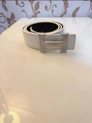 Vitt H bälte  - Säljer ett vitt bälte med ett H på. Det är i nyskick den är 105cm lång och är justerbar. Priset går att diskuteras vid snabb affär. Skickar inom 24h!