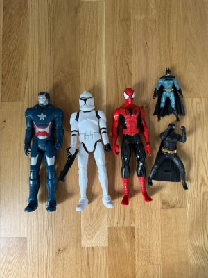 Superhjälte actionfigurer 5-pack - Säljer ett set med fem actionfigurer: Captain America i blått och rött, en vit Star Wars stormtrooper med vapen, Spider-Man i rött och svart samt två olika Batman-figurer i svart och blått med cape. Perfekt för dig som gillar Marvel och DC!