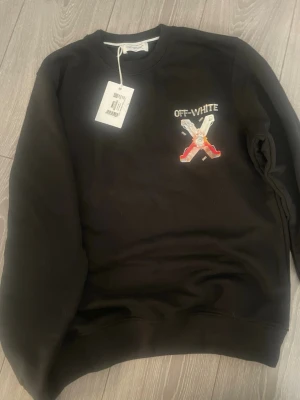 Svart sweatshirt från Off-White - Svart sweatshirt från Off-White med broderad logga och X-motiv på bröstet. Rund halsringning och ribbade muddar. Perfekt för en streetwear-look och enkel att matcha med jeans eller cargo.