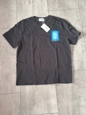 Svart t-shirt från Casablanca - Snygg svart t-shirt från Casablanca med tryck i blått och vitt på bröstet. Klassisk rund hals och korta ärmar. Tillverkad i mjuk bomull för en skön känsla. Perfekt för dig som gillar stilrena plagg med en twist.