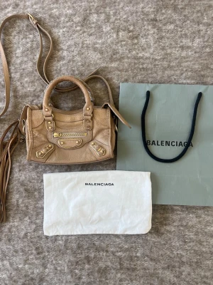 Trendig snygg Balenciaga city bag mini  - Otroligt fin väska. Originalpåse, dustbag och långt band ingår. Har dessvärre inget kvitto kvar. Den är i gott skick och har varit välomhändertagen, men skinnet och guldnitar har normalt slitage och tecken på användning ( se bilder) samt en fläck på baksidan ( sista bild). Skriv gärna för fler bilder på något 
