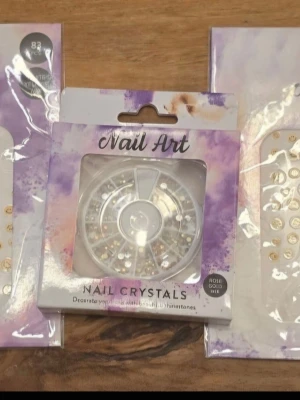 Nail Art  - Säljer ett set med Nail Art kristaller och dekorationer för naglar. Innehåller blandade stenar i olika former och storlekar, främst i roséguld och klara färger.2 förpack med nageldekorations klistermärken.
