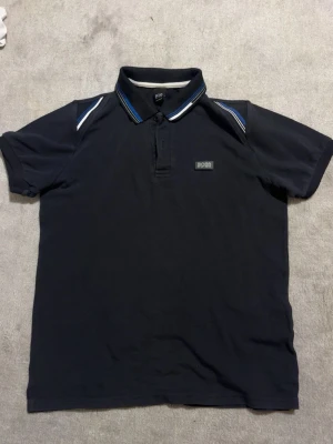 Hugo Boss pikétröja mörkblå – Strl M - Säljer en Hugo Boss pikétröja i mörkblå färg med stilrena detaljer på krage och axlar. Klassisk och tidlös modell som passar både till vardags och finare tillfällen.📏 Storlek: M ✅ Fint skick ✅ Original Hugo Boss ✅ Broderad/metall-logga på bröstet ✅ Bekväm passform