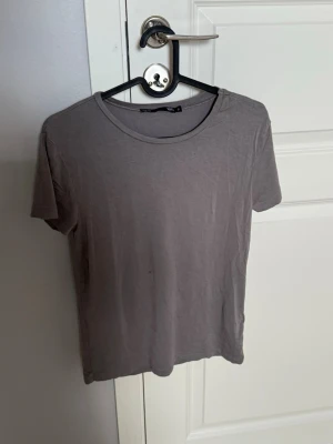 Grå basic t-shirt - En enkel grå t-shirt med rund hals och korta ärmar. Perfekt till jeans eller shorts för en clean och avslappnad look. Tillverkad i mjuk bomull som känns skön mot huden.