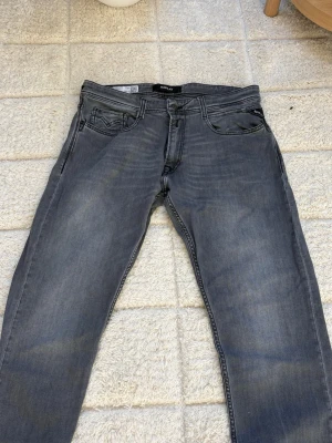 Replay Rocco  - Säljer ett par gråa jeans från Replay med klassisk femficksmodell och snygga detaljer på bakfickorna. Jeansen har en rak passform och är tillverkade i mjukt denimtyg som ger en avslappnad look. Perfekta för dig som gillar streetwear och stilrena plagg.