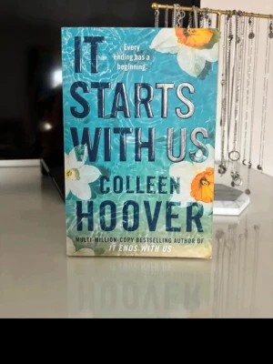 It Starts With Us av Colleen Hoover - En skönlitterär bok med titeln 'It Starts With Us' av Colleen Hoover. Boken är på engelska och handlar om relationer, kärlek och nya början. Perfekt för dig som gillar romantik och drama. Är lite sliten!