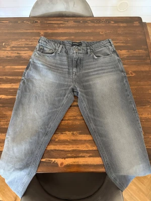 Grå straight fit jeans från River Island  - Säljer ett par gråa straight fit jeans från River Island med klassisk femficksmodell och normal midja. Jeansen har en snygg tvättad look och är tillverkade i bomull. Passar perfekt till en avslappnad stil och har diskreta detaljer på bakfickan. Köpta i Nordirland för ≈600kr och säljer med lapp fortfarande på då jag fick med mig fel storlek hem. W34 men sitter närmre 32 skulle jag säga.
