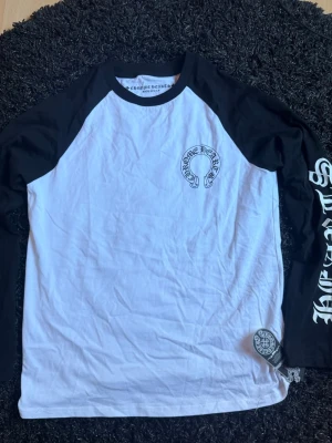 Chrome Hearts långärmad t-shirt - Säljer en svartvit långärmad t-shirt från Chrome Hearts med kontrastärmar och tryck på bröstet, ärmarna och ryggen. Klassisk baseballmodell med cool grafik och logga. Perfekt för dig som gillar streetwear och vill sticka ut.