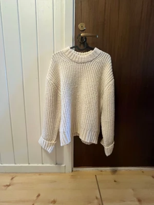 Vit stickad tröja - Säljer en vit oversized stickad tröja från lager med ribbstickning och bred polokrage. Tröjan har nedhasade axlar, långa ärmar med uppvikta muddar och en avslappnad passform. Perfekt för kalla dagar och enkel att styla till olika outfits. Har aldrig använt den har bara hängt i garderoben.