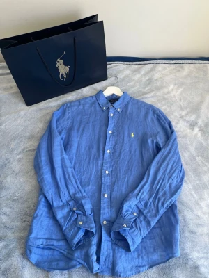 💙Blå linneskjorta från Polo Ralph Lauren - Snygg blå 💙skjorta från Polo Ralph Lauren i linne med klassisk button-down krage och broderad gul logga på bröstet.Perfekt för en avslappnad men stilren look.🔥 skriv vid minsta intresse. Priset är  inte hugget i sten 🪨 