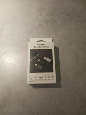 Smart Remote Control USB-adapter - Smart Remote Control är en liten USB-adapter som gör det möjligt att styra TV, AC, kamera, glödlampa och fläkt via mobilen. Kompakt design i svart och vitt, passar direkt i telefonens port. Perfekt för dig som vill ha kontroll över flera prylar med en enda enhet.