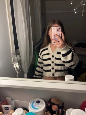 Randig stickad kofta från H&M - Den här randiga koftan är perfekt för både vardag och finare tillfällen. Modellen är kort/croppad med knappar framtill och lång ärm – superenkel att styla både öppen och knäppt. Ger en clean, chic look som funkar året runt. Knappt använd – i mycket fint skick, inga fläckar, noppor eller slitage.