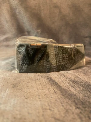 Louis Vuitton svart monogram bälte - Snyggt svart bälte från Louis Vuitton med klassiskt monogrammönster och stor LV-logga i metall framtill. Bältet är gjort i läder med detaljer i canvas och har en stilren design som passar till många outfits.