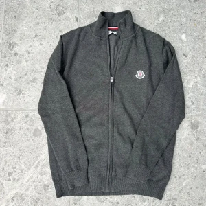 Mörkgrå kofta med dragkedja från Moncler - Säljer en mörkgrå kofta från Moncler med hel dragkedja framtill och broderad logga på bröstet. Tröjan är i nyskick,inga skador eller nåt sånt den passar även för M beroende på vikt osv, priset är ej hugget i sten så skriv vid funderingar🙌