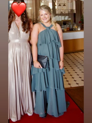 Grön volangklänning med halterneck - Säljer min älskade balklänningen från veromoda. Det är långklänning med volanger och halterneck. Endast använd 1 gång i 2 timmar och i fint skick, säljer pgr av att jag tyvärr inte har nått tillfälle att ha den till. Skriv gärna privat om du har frågor eller undrar över nått!