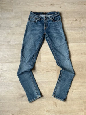 Blåa Nudie Skinny Sam Jeans - Fina Nudie Jeans i blå färg.| Jeansen är i mycket bra skick och sparsamt använda.|  Äkta som allt annat jag säljer! ✅|  Storlek: W26 L32| Skick: Mycket Bra Skick| Färg: Blå| Märke: Nudie|| Modell: Jeans |  Hör gärna av dig vid frågor så svarar jag så fort jag kan! 😁|   SKU - 9