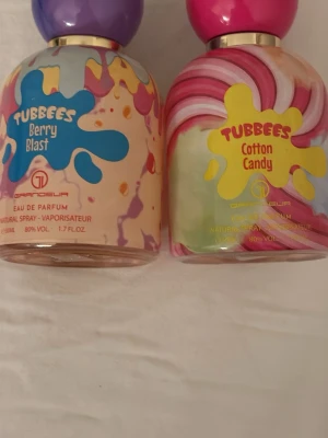 Tubbees parfymduo Berry & Cotton - Två färgglada parfymer från Grandoeur: Tubbees Berry Blast med lila lock och blå etikett samt Tubbees Cotton Candy med rosa lock och gul etikett. Flaskorna har lekfulla mönster i pastellfärger och rymmer 50 ml vardera. Perfekt för dig som gillar söta och fruktiga dofter.