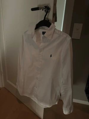 Vit skjorta från Polo Ralph Lauren - Klassisk vit skjorta från Polo Ralph Lauren i slim fit-modell. Skjortan har knappar framtill, lång ärm och den ikoniska broderade loggan på bröstet. Tillverkad i mjuk bomull som känns skön mot huden. Perfekt för en clean och stilren look. Kom privat vid eventuella frågor eller för bättre bilder!😀