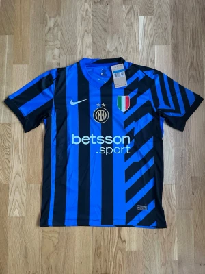 Inter Milan matchtröja Nike blå/svart - Snygg Inter Milan matchtröja från Nike i blått och svart med grafiskt mönster. Tröjan har klubbmärke, sponsortryck och italienska mästarmärket på bröstet. Korta ärmar och lätt, ventilerande material perfekt för fotbollsträning eller match.
