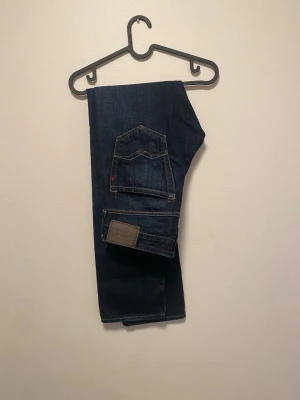 Mörkblå jeans från Replay - Snygga mörkblå jeans från Replay med klassisk femficksdesign och kontrastsömmar. Jeansen har en rak passform och är tillverkade i slitstark denim. Perfekta för dig som gillar stilrena och tidlösa plagg.