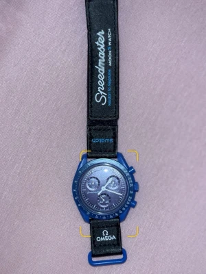 Omega x Swatch Speedmaster blå klocka - Säljer en blå Omega x Swatch Speedmaster MoonSwatch Mission to Neptune. Klockan har svart textilarmband med vita och blå detaljer, rund urtavla med kronograf och tydliga index. Snygg och sportig design som sticker ut på handleden.