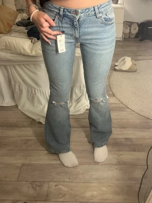 Ljusblå bootcut jeans med slitningar - Säljer ett par ljusblå bootcut jeans med slitningar vid knäna och klassisk femficksdesign. Jeansen har lägre midja och är tillverkade i denim med en snygg tvätt. Perfekta för en avslappnad och trendig look. Storlek S full length