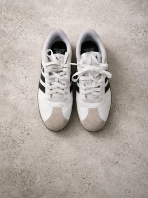 Vita Adidas sneakers med svarta ränder - Snygga vita sneakers från Adidas med klassiska svarta ränder på sidorna. Lite smutsig men går att tvätta