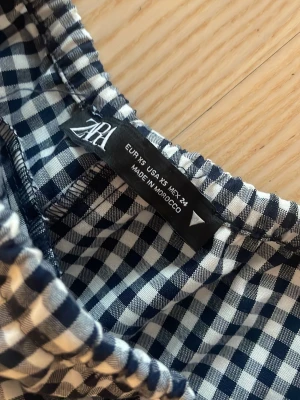 Rutiga shorts från Zara med snörning - Snygga blåvita rutiga shorts från Zara med elastisk midja och vit snörning framtill. Perfekta för sommardagar och har en avslappnad passform. Tillverkade i ett mjukt bomullsmaterial som känns skönt mot huden.