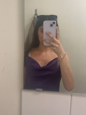 Lila linnetopp med cowlneck - Snygg lila linnetopp med cowlneck och tunna axelband. Perfekt att styla med smycken och jeans för en trendig look. Toppens material har en lätt glansig finish som ger en lyxig känsla.